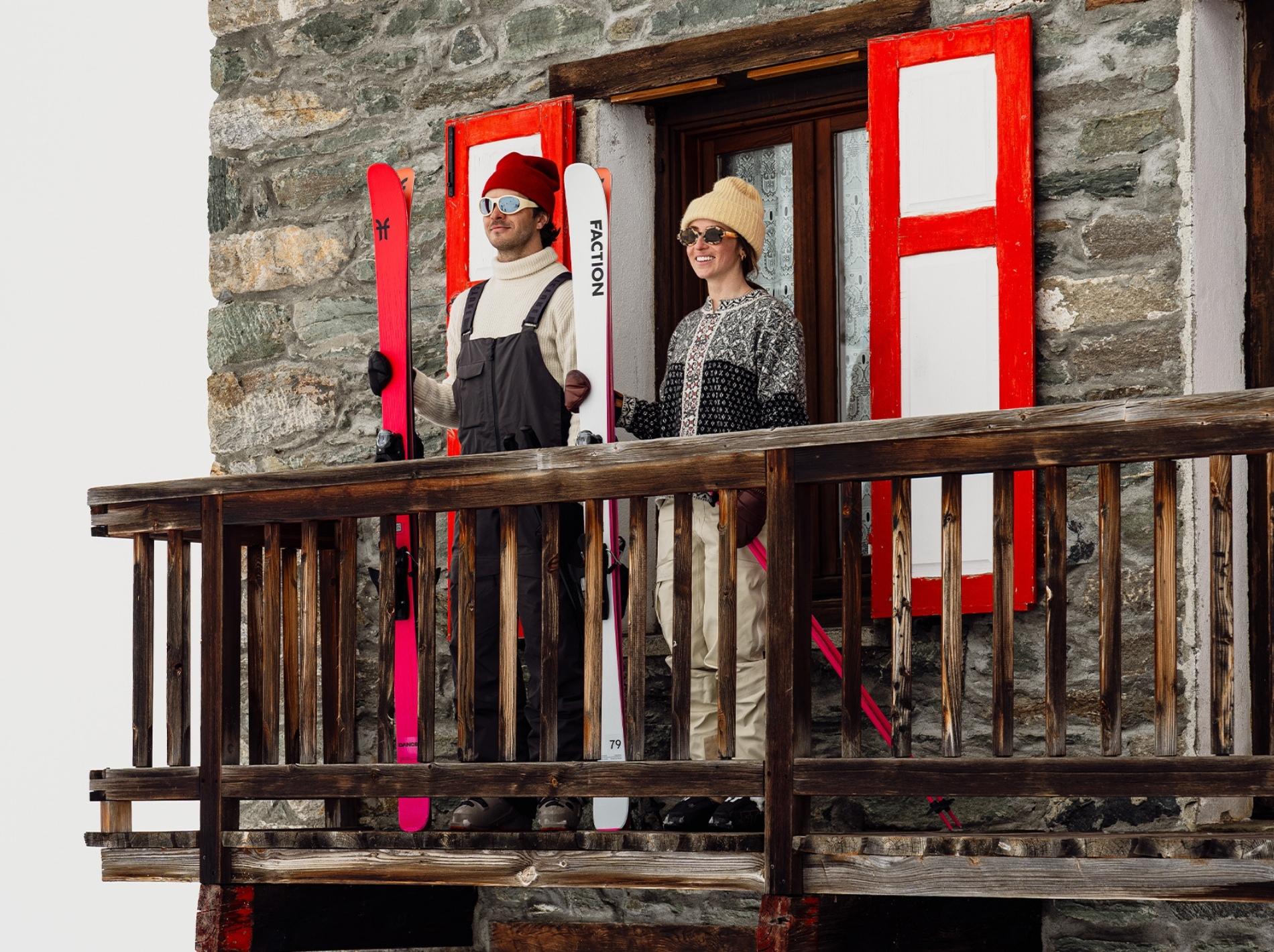 Two skiers stood on a balcony with Faction skis